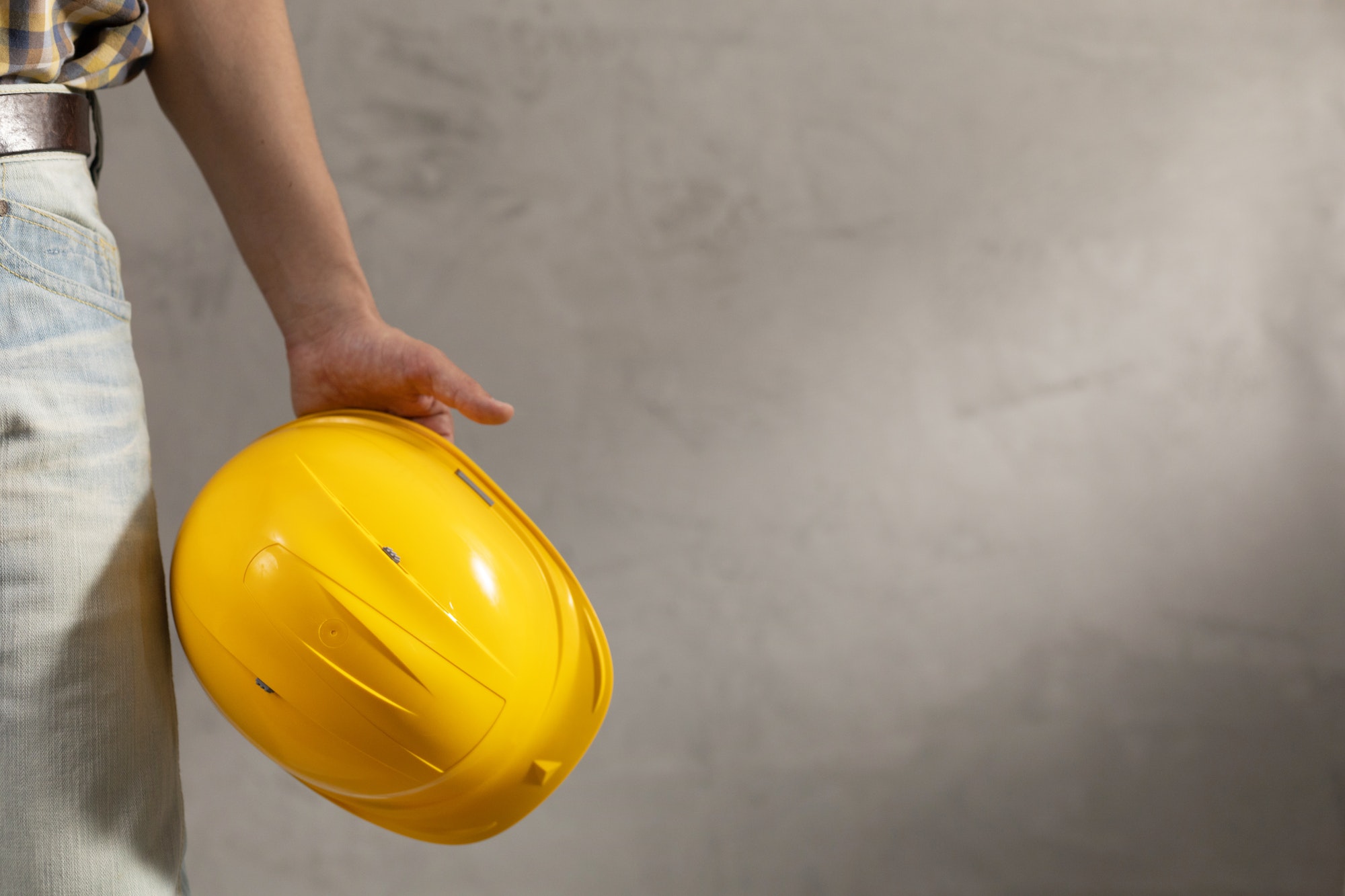 Worker man holding construction helmet tool near concrete or cement wall. Male hand and work cap